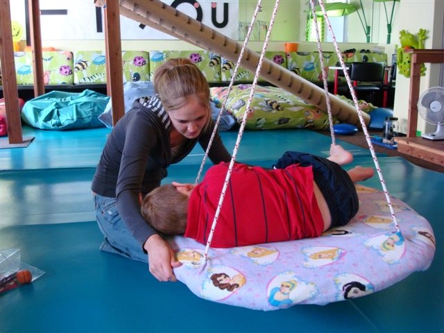 Occupational therapy personnel working with child side-lying on round platform swing